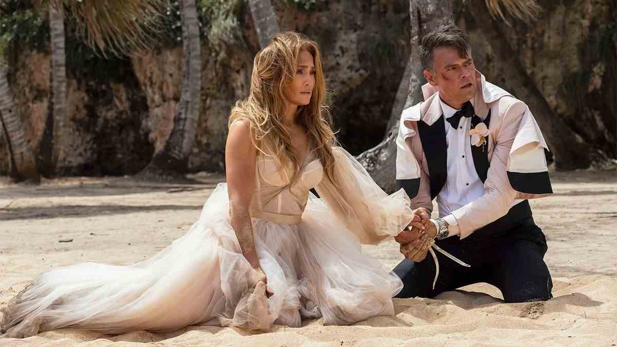 Une femme en robe de mariée déchirée (Jennifer Lopez) s'agenouille sur une plage à côté d'un homme (Josh Duhamel) en smoking en lambeaux avec une ecchymose ensanglantée sur la joue.