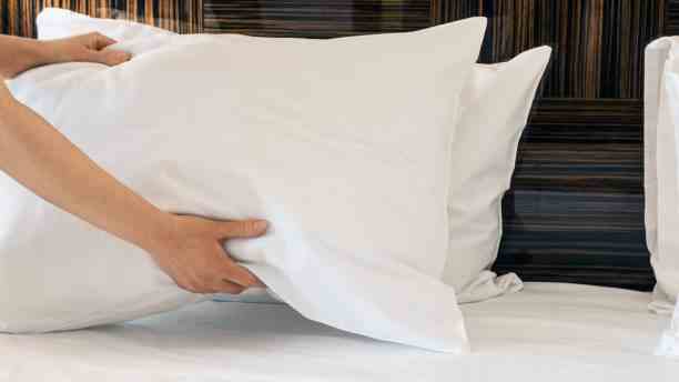 Une personne place deux oreillers blancs sur un lit