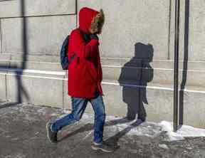 Un piéton tient son capot fermé en marchant sur le boul. René-Levésque.  par une journée extrêmement froide et venteuse à Montréal le vendredi 3 février 2023.