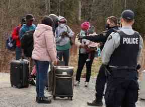 Les demandeurs d'asile parlent à un policier alors qu'ils traversent le Canada depuis la frontière américaine près d'un point de contrôle sur le chemin Roxham près de Hemmingford, Québec, le 24 avril 2022. REUTERS/Christinne Muschi