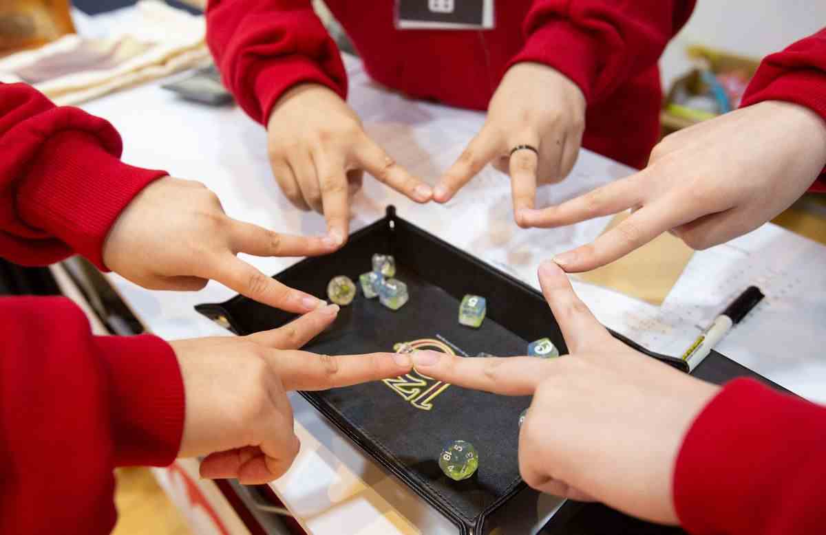 Trois joueurs font un signe semblable à un pentagramme avec leurs doigts sur un plateau de dés dans un jeu de Call of Cthulhu.  Ils portent tous des pulls molletonnés.