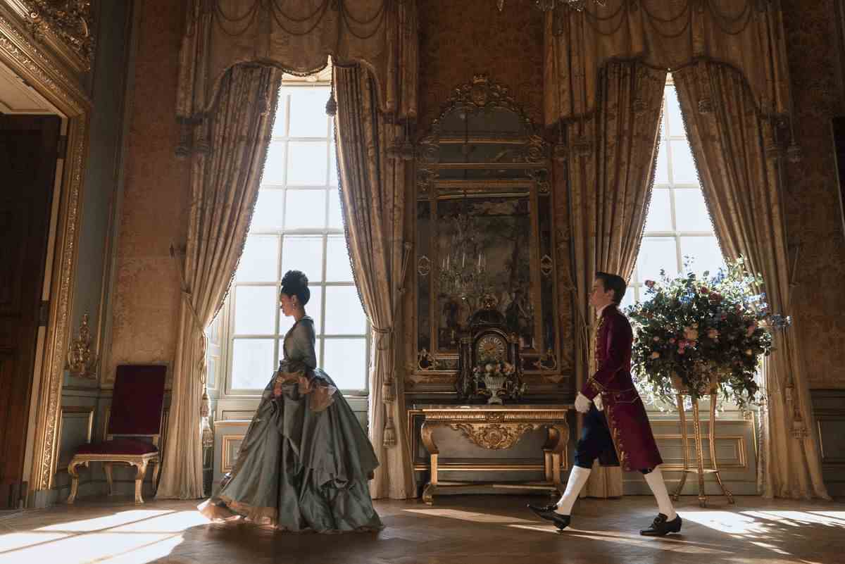 la jeune reine charlotte se promène dans les salles chics du palais, un domestique la suivant