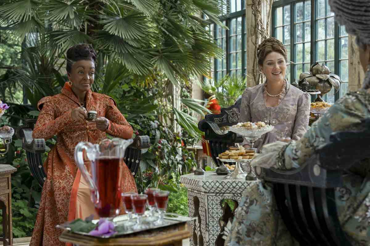 lady danbury, une femme noire vêtue d'orange, et lady bridgerton, une femme blanche en lilas, sourient à la reine lors d'une garden-party