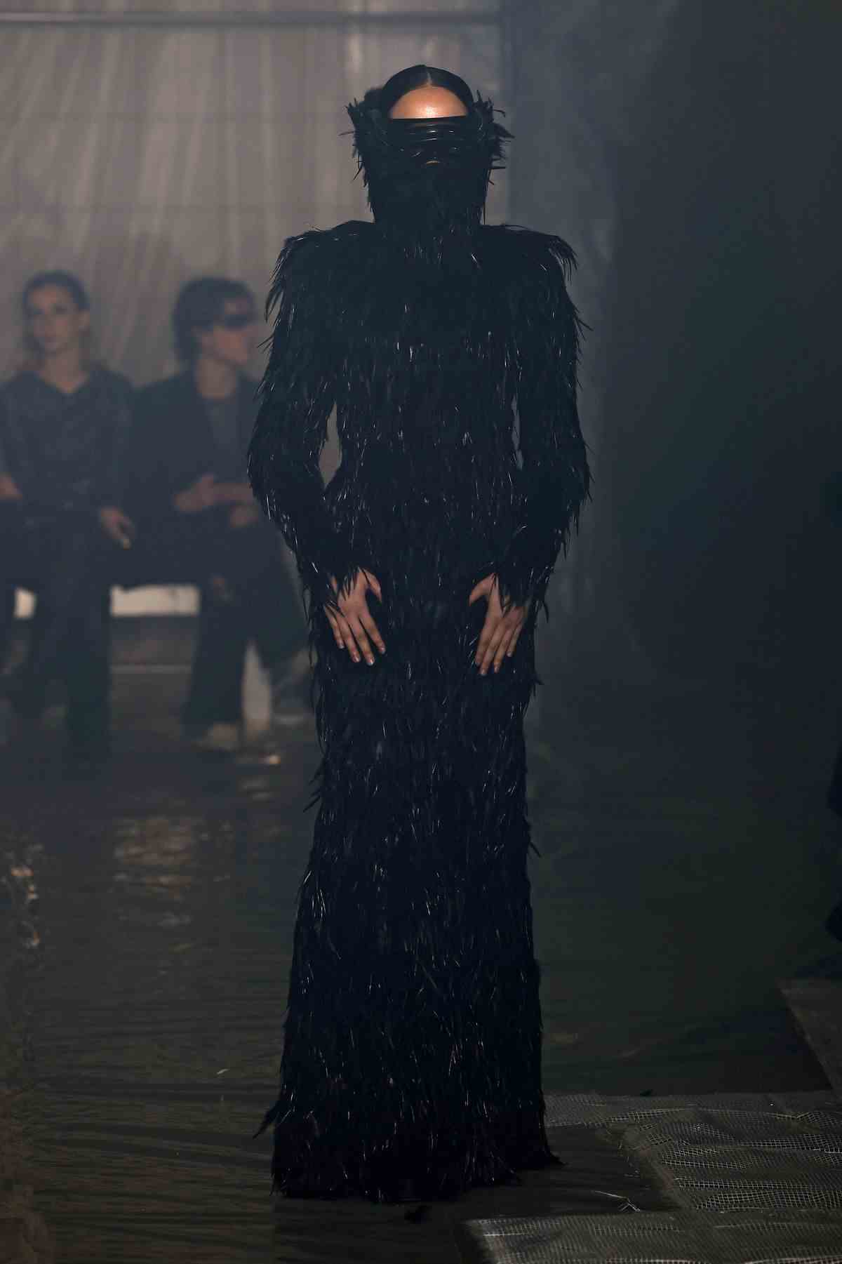Un mannequin portant une longue robe noire à plumes et des lunettes de soleil masquant le visage défile lors du défilé de mode Han Kjobenhavn à la Fashion Week de Milan.