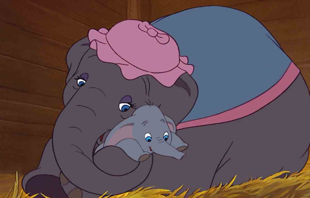 Mme Jumbo, un éléphant coiffé d'une casquette rose et d'un châle bleu, berce son bébé Dumbo dans sa malle alors qu'elle est allongée dans un lit de paille dans le long métrage d'animation Dumbo de 1941