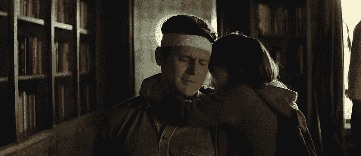 Attaché à une chaise et avec un bandage autour de la tête, l'otage Eric (Jonathan Groff) se penche dans une étreinte de sa fille Wen (Kristen Cui) dans Knock at the Cabin