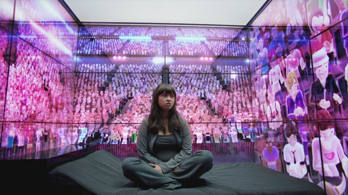 Une femme est assise dans une pièce entourée de murs d'avatars informatiques assis dans un grand auditorium.