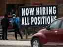 Une personne debout près d'un panneau indiquant qu'une entreprise locale embauche.