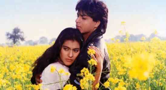 A man in a black leather jacket and a woman in a white Indian salwar-kameez hug in a field surrounded by yellow flowers; still of Kajol and Shah Rukh Khan in "Dilwale Dulhania Le Jayenge"