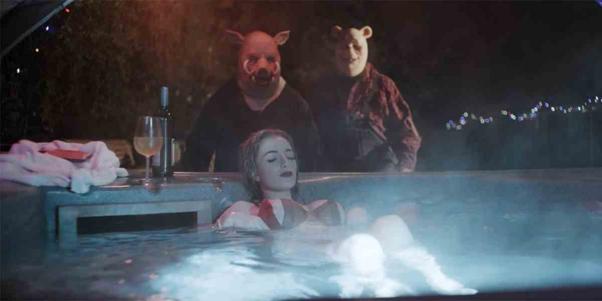 Une femme en bikini (Natasha Tosini) se prélasse les yeux fermés dans un bain à remous extérieur la nuit tandis que les tueurs Pooh (Craig David Dowsett) et Piglet (Chris Cordell) se faufilent derrière elle dans Winnie the Pooh: Blood and Honey