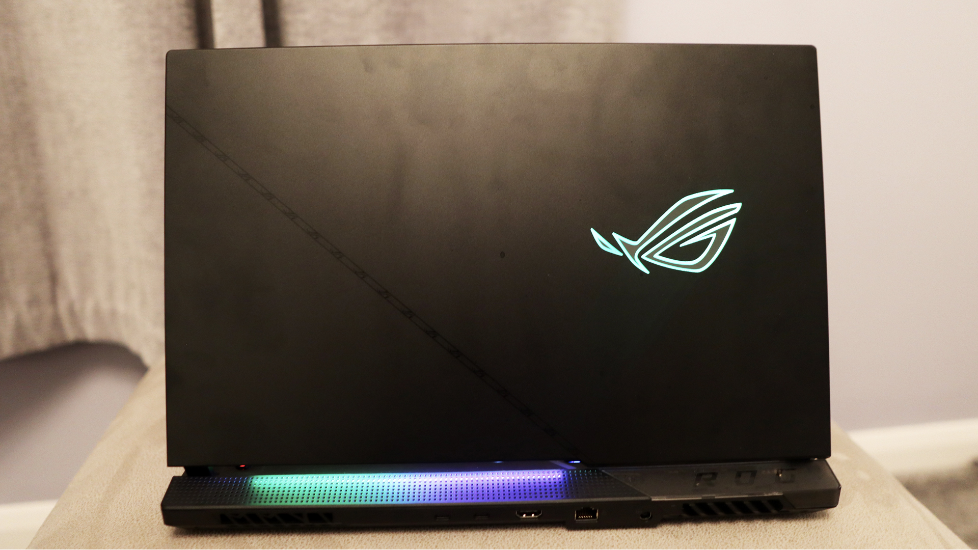 Asus ROG Strix Scar 17 review : Un ordinateur portable de jeu placé sur un support beige, son châssis en plastique éclairé par un logo RVB