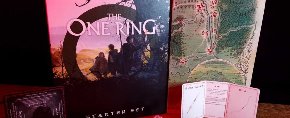 The One Ring Starter Set box, map, cards, and dice on a wooden table against a dark backdrop