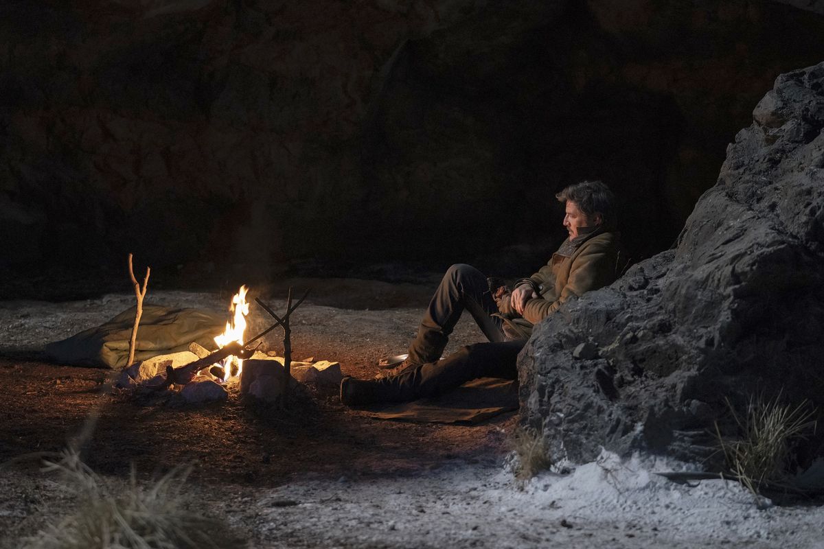 Joel (Pedro Pascal) assis et appuyé contre une paroi rocheuse et regardant un feu