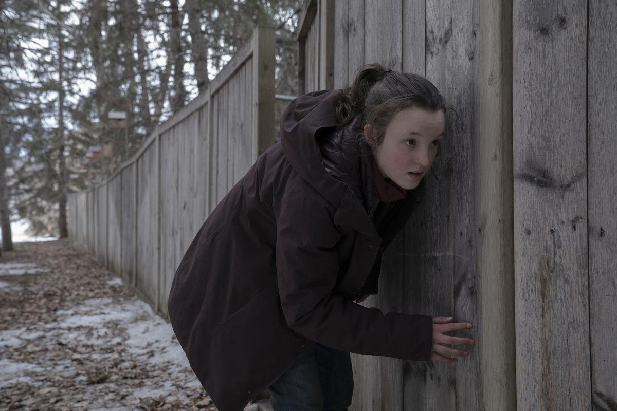 Ellie s'accroupit et se presse contre une clôture en bois en hiver dans une scène de The Last of Us de HBO