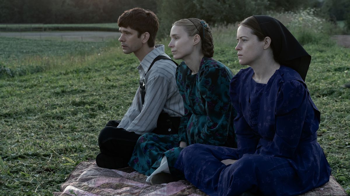 Un homme (Ben Whishaw), une femme (Rooney Mara) et une autre femme (Claire Foy) sont assis sur une couverture surplombant un champ d'herbe verte.