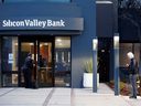 Un employé de banque attend d'être laissé entrer alors qu'un client fait la queue devant le siège social de la Silicon Valley Bank à Santa Clara, en Californie.