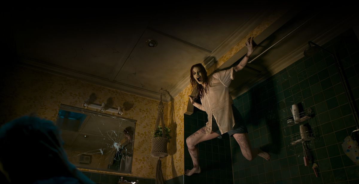 Deadite Ellie (Alyssa Sutherland), nouvellement possédée, siffle à travers une bouche noircie tout en s'accrochant à un mur dans son appartement sombre dans Evil Dead Rise