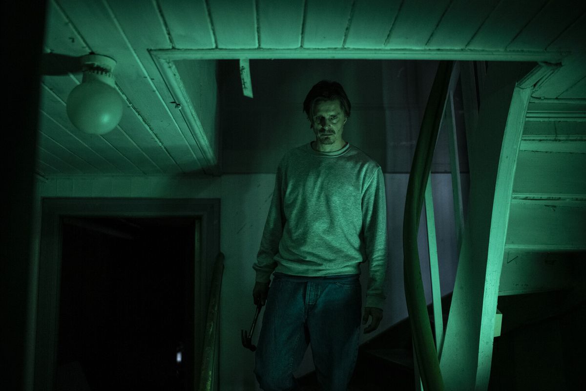 Un homme à l'allure nordique tient un marteau sur un escalier avec un éclairage vert en congé.
