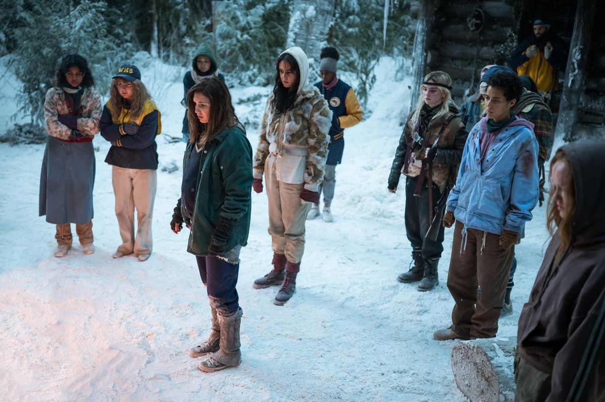Les adolescents Yellowjackets se tiennent dans la neige à l'extérieur de leur cabine, avec un feu de camp juste hors écran lors de la première de la saison 2 de Yellowjackets.