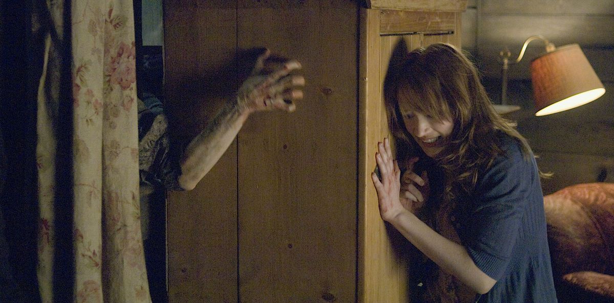 Dana (Kristen Connolly) pousse une grande armoire en bois contre une fenêtre brisée alors que des zombies tentent de se frayer un chemin dans sa cabane rustique dans The Cabin in the Woods de 2011