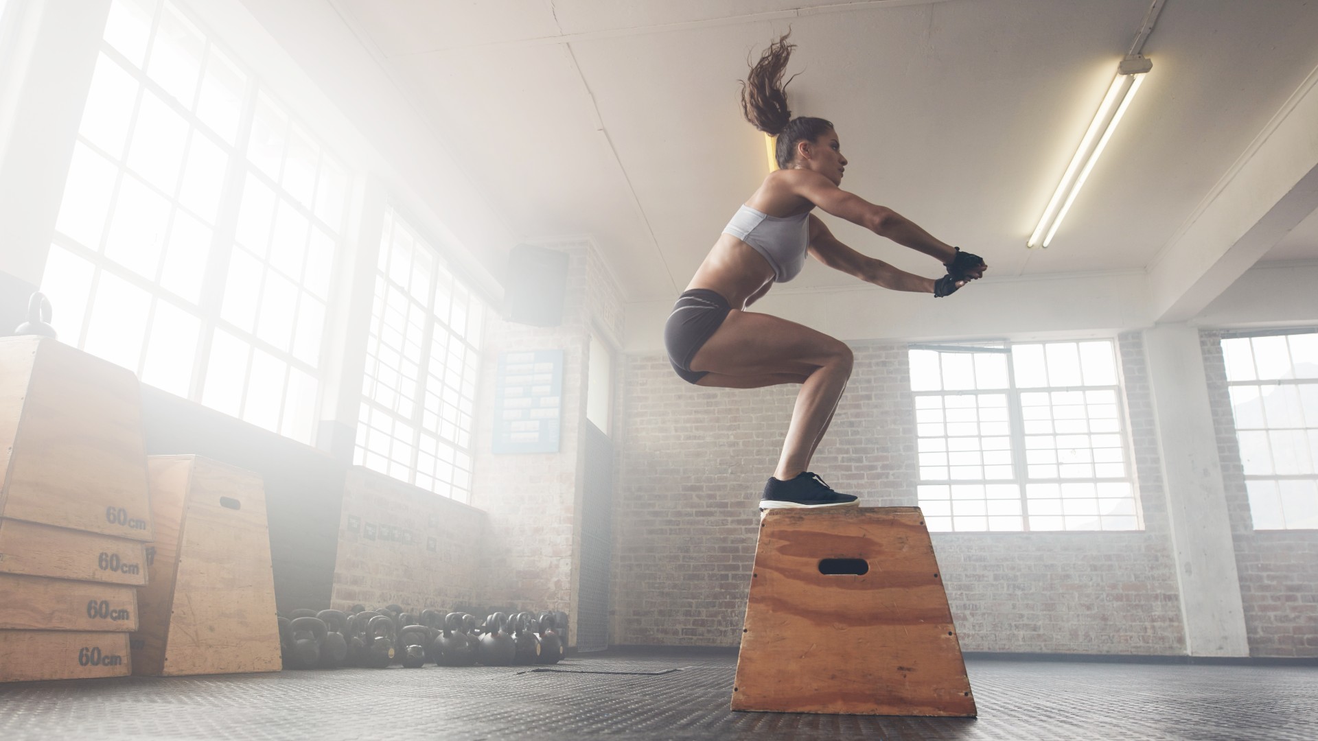 Femme exécutant un saut de boîte dans un entrepôt de gym atterrissant avec les deux pieds sur une boîte pendant l'entraînement de poids corporel