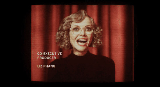 Medium shot of a woman with curly blonde hair and glasses laughing maniacally in front of a red curtain backdrop; still of Christina Ricci in "Yellowjackets"