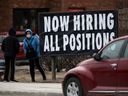Une personne debout près d'un panneau indiquant qu'une entreprise locale embauche à Winnipeg.  