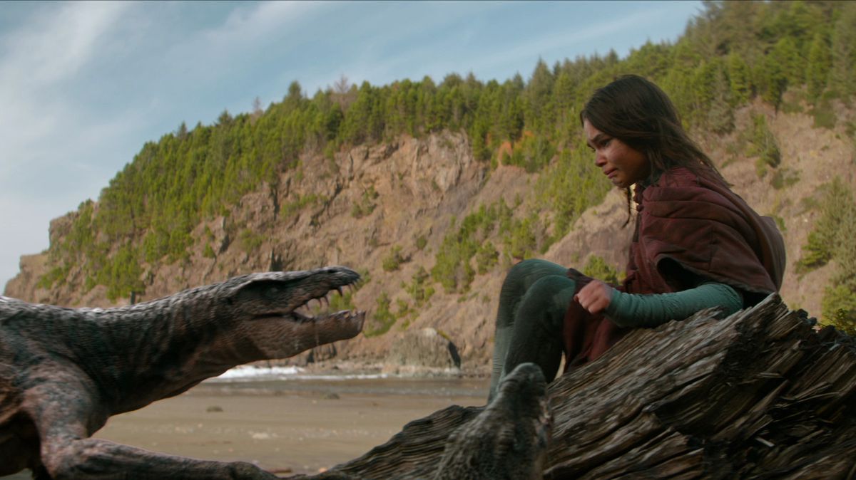 Un dinosaure ressemblant à un lézard siffle à l'adolescente brune qui recule lentement sur un rocher dans le film 65