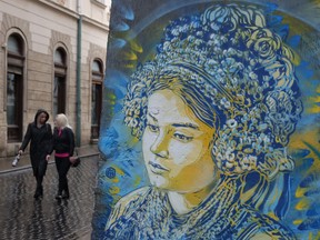 Des femmes passent devant une peinture murale dans le bleu et le jaune du drapeau ukrainien représentant une femme en tenue folklorique traditionnelle à Lviv, en Ukraine.  Bien que Lviv, située dans l'ouest de l'Ukraine, soit loin des combats actuels qui font rage entre les forces armées ukrainiennes et russes à l'est et offre même un sentiment de normalité dans la vie quotidienne, elle reste néanmoins profondément affectée par la guerre.