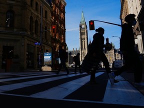 Le drapeau du Canada flotte sur la tour de la Paix de la colline du Parlement alors que les piétons se frayent un chemin le long du centre commercial de la rue Sparks à Ottawa, le 9 novembre 2021. Les fonctionnaires fédéraux devraient reprendre leurs fonctions d'ici la fin du mois.