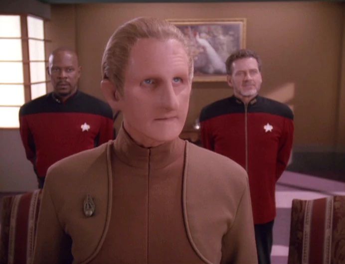 Le gendarme Odo, membre de la race Changling dans Star Trek: Deep Space 9. Il est flanqué du capitaine Sisko d'un côté et d'un amiral de Starfleet de l'autre. 