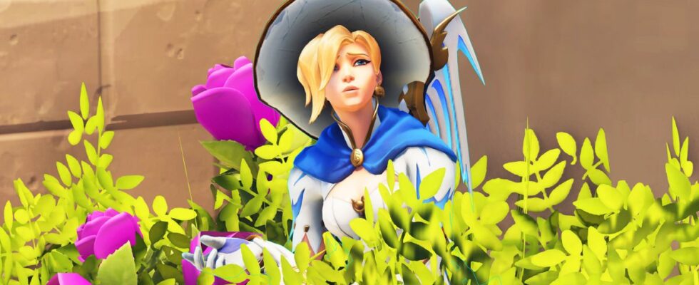 Mercy from Overwatch hiding in a bush. She is shrugging. She seems confused.