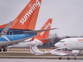 Un petit avion passe devant des Boeing 737 appartenant au transporteur aérien Canadian Vacation Sunwing assis sur le tarmac de l'aéroport international de Waterloo à Waterloo, en Ontario, le 24 mars 2020.