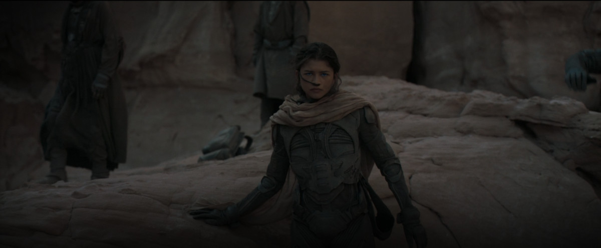 Inalan (Zendaya) se tient dans la pénombre contre un affleurement de rochers dans une image de Dune 2021 de Denis Villeneuve