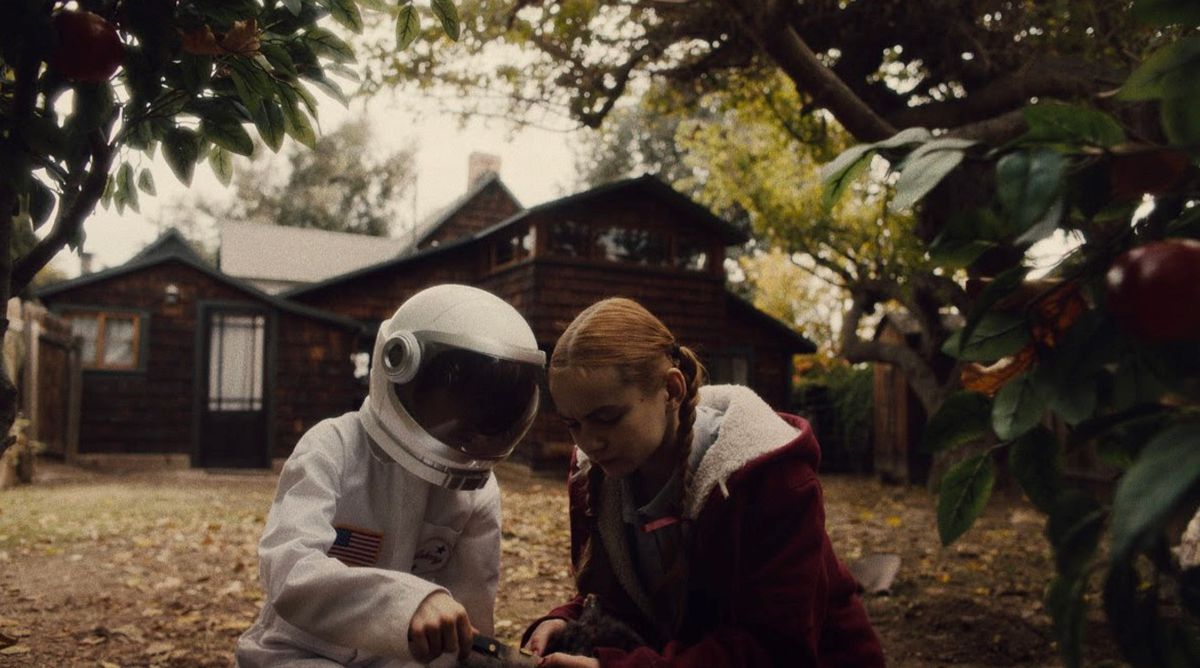 Une jeune fille est assise à côté d'un jeune garçon vêtu d'un costume d'astronaute devant une maison dans Spoonful of Sugar.