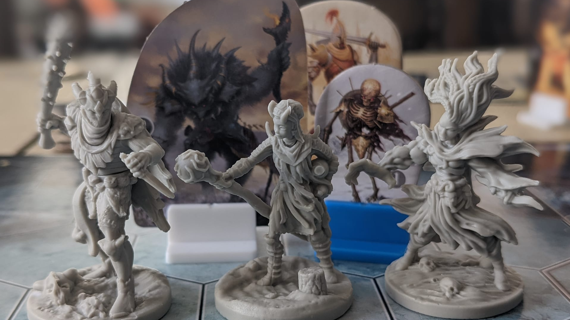 Trois figurines de Frosthaven sont alignées sur un tableau devant des monstres en carton