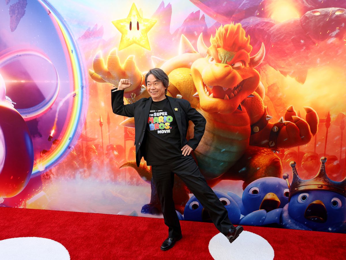 Shigeru Miyamoto posant sur le tapis rouge lors de la première de The Super Mario Bros. Movie LA.  Il porte un costume noir et un t-shirt Super Mario Bros. Movie.