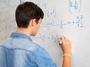 Un élève résout un problème mathématique sur un tableau blanc dans une salle de classe.