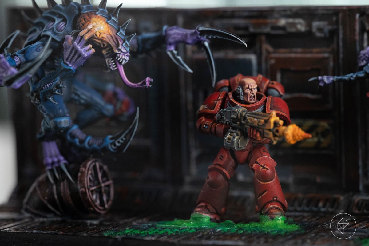Deux tyranides flanquent une figurine Space Marine blindée rouge.  Le sol de ce space hulk est recouvert d'un ichor vert vif.