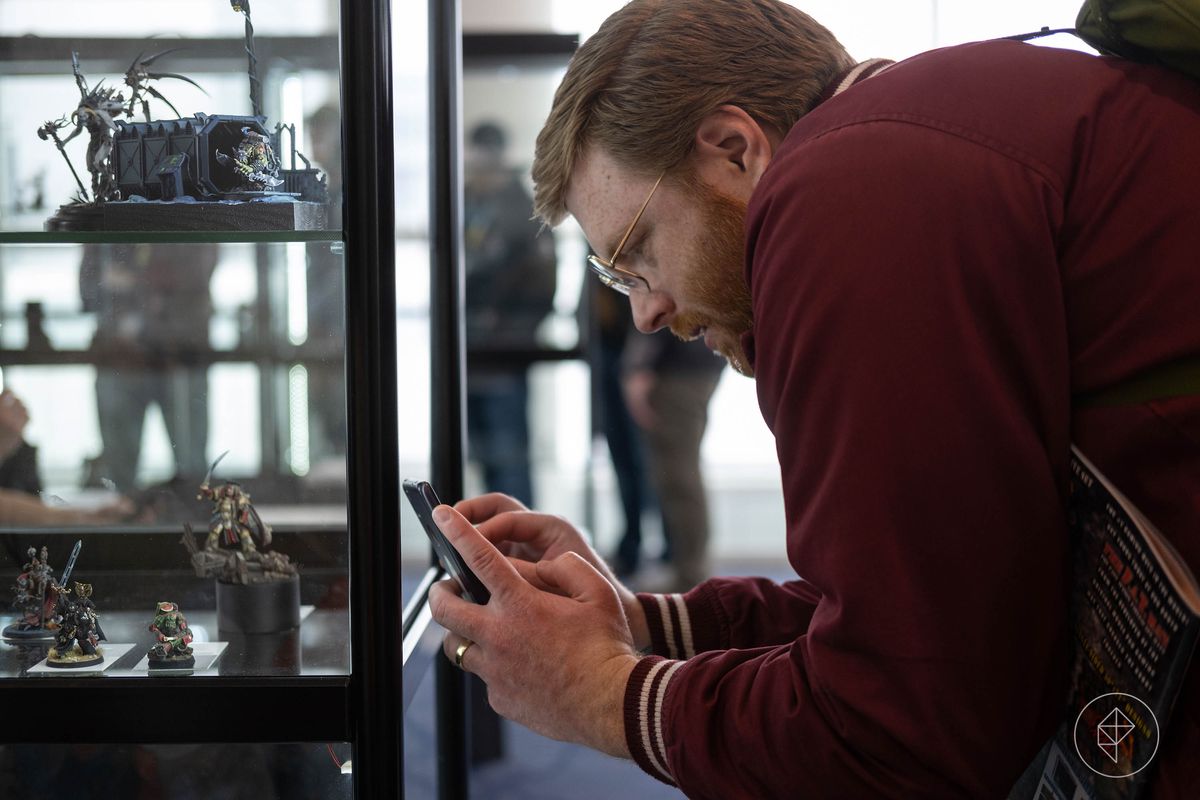 Un homme aux cheveux roux avec un téléphone portable prend des photos des miniatures exposées au Golden Demon.