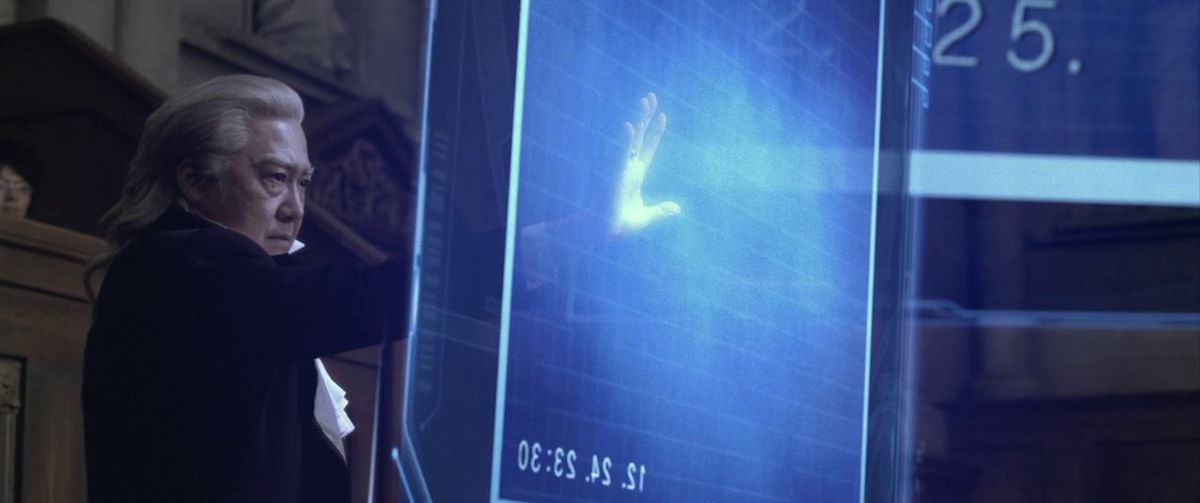 Un procureur tend la main pour toucher un écran holographique géant dans l'adaptation en direct d'Ace Attorney.
