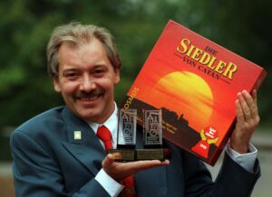 Klaus Teuber, tenant une première version de Catan et ses prix Spiel des Jahres en 1995.