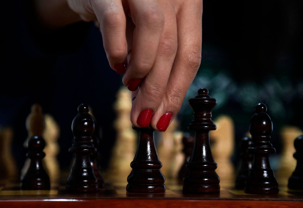 Doigts touchant une pièce d'échecs.  Les ongles sont peints en rouge.