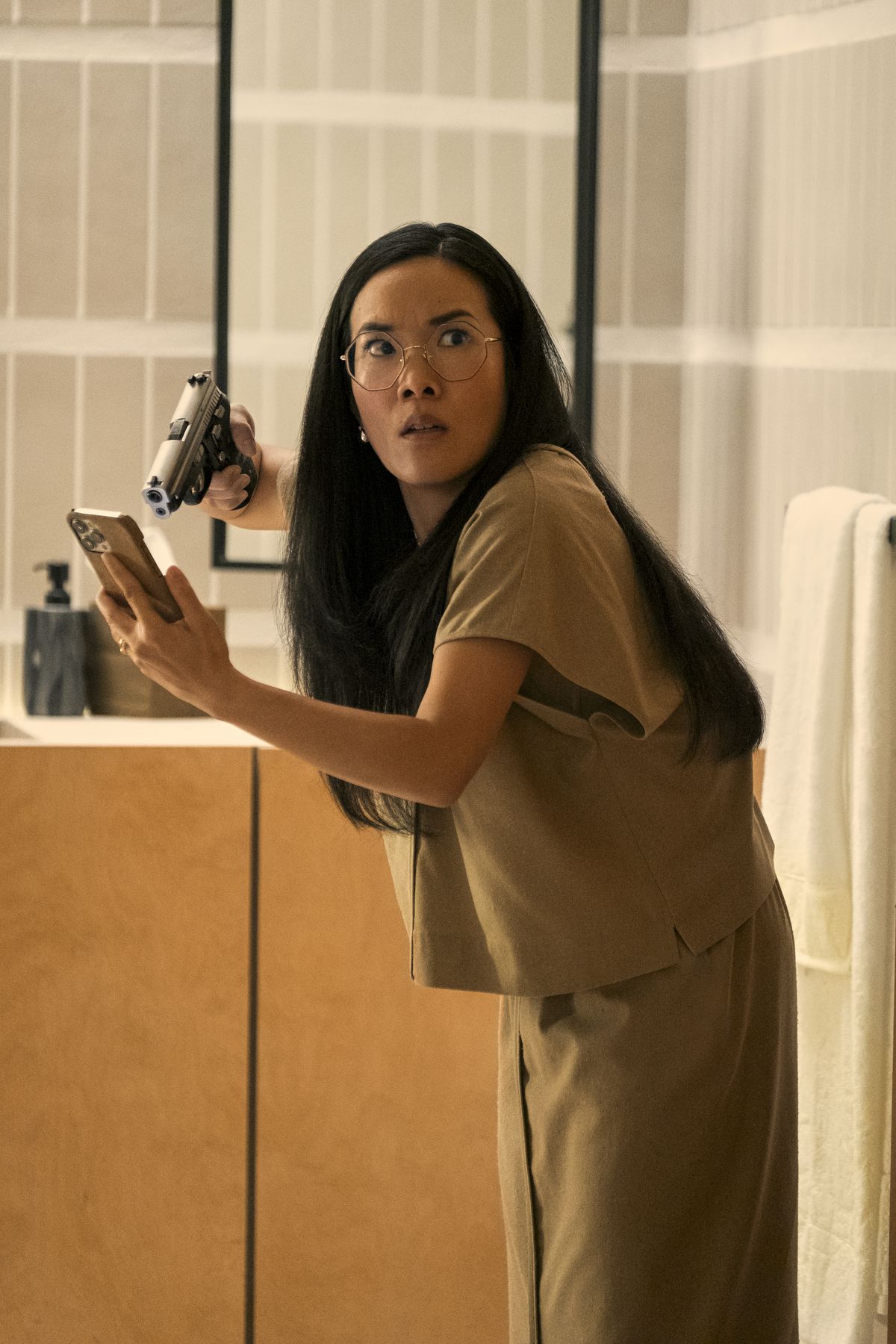Amy (Ali Wong) tient une arme à feu sur un téléphone dans sa main et a l'air choquée par quelque chose hors champ