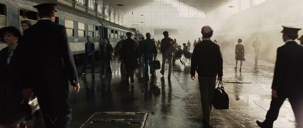 Des passagers transportant des valises marchent le long d'un train dans une gare éclairée par des fenêtres lumineuses soufflées, projetant chaque personne en silhouette à Munich 