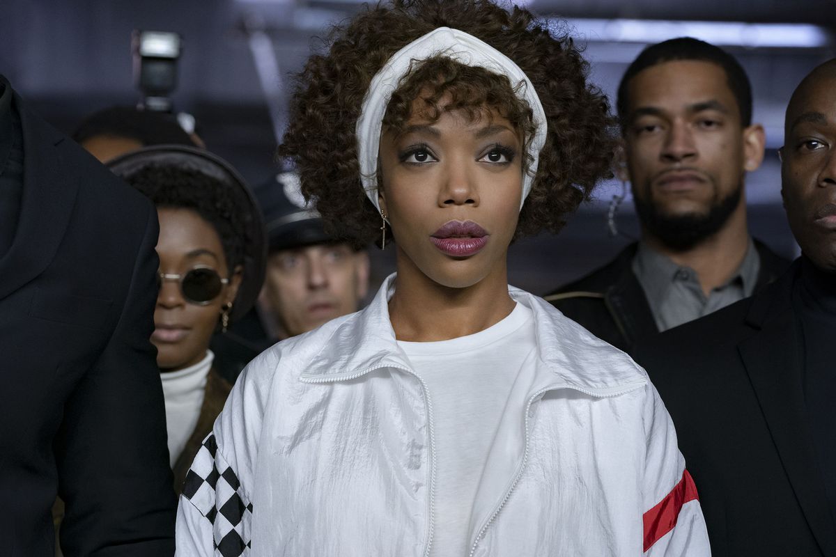 Naomi Ackie est vêtue de blanc, avec un bandeau blanc, et est entourée d'agents de sécurité comme Whitney Houston dans I Wanna Dance With Somebody.