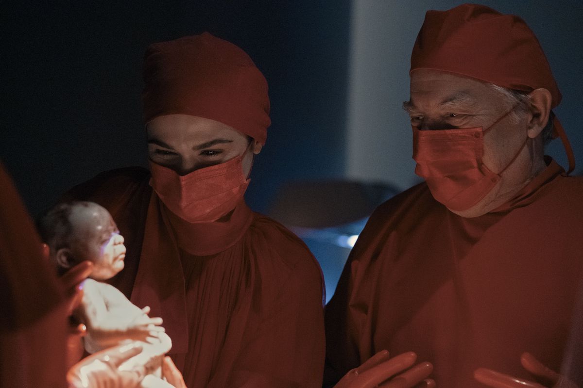 Elliot Mantle (Rachel Weisz) tenant un nouveau-né avec un autre médecin (Michael McKean) regardant par-dessus son épaule