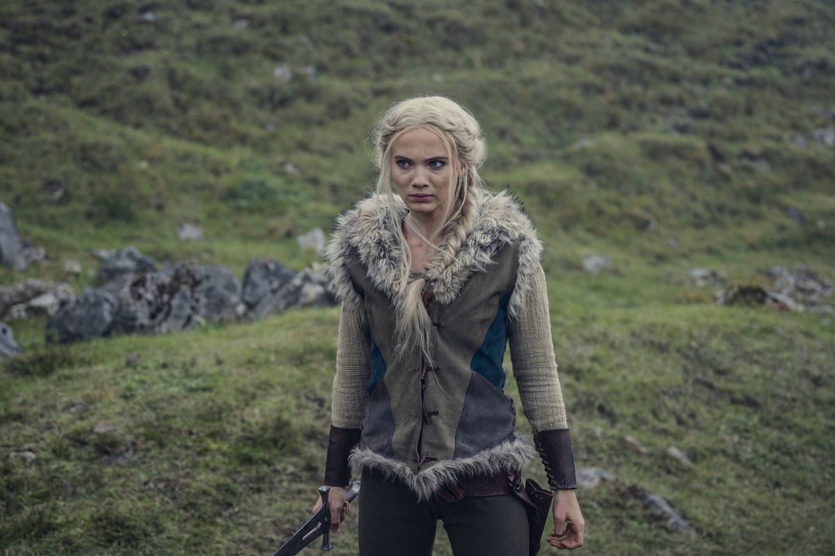 Freya Allen dans le rôle de Ciri dans la saison 3 de The Witcher de Netflix se tient face à la caméra sur une colline herbeuse avec une épée à la main
