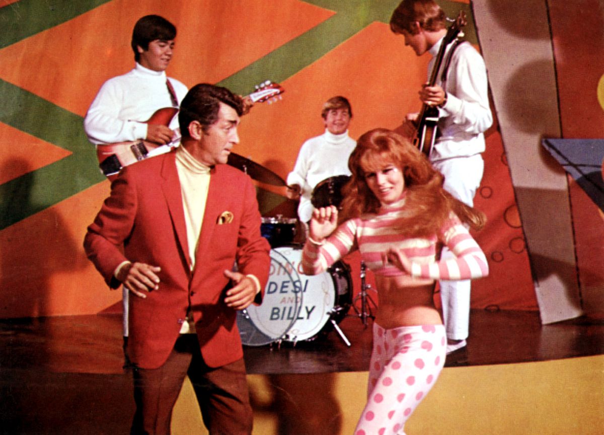 Matt Helm en costume rouge danse avec une fille rousse devant le groupe Desi and Billy
