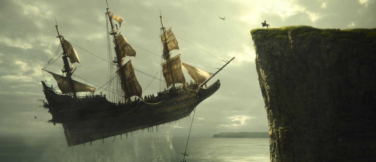 Un navire volant avec des voiles plane au-dessus de l'eau et s'approche d'une falaise, où un personnage est assis sur un cheval dans Peter Pan et Wendy.